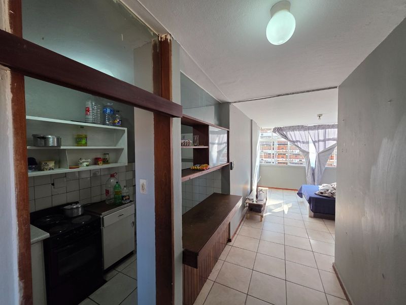Open plan apartment layout featuring a compact kitchen with built-in stove and oven, leading into a living area with tiled flooring throughout.