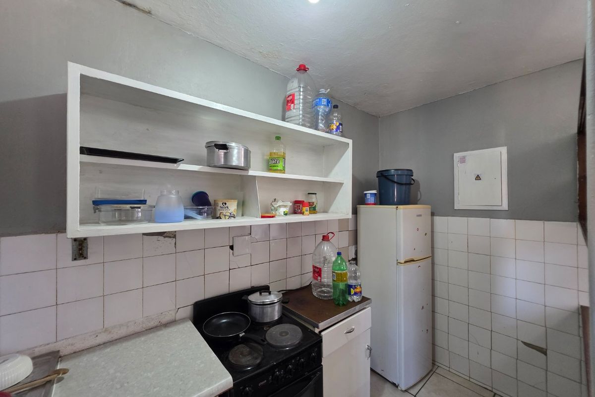 A compact kitchen featuring tiled splashbacks, built-in shelving, and an electric stove, requiring cosmetic updates to improve its overall condition and functionality.