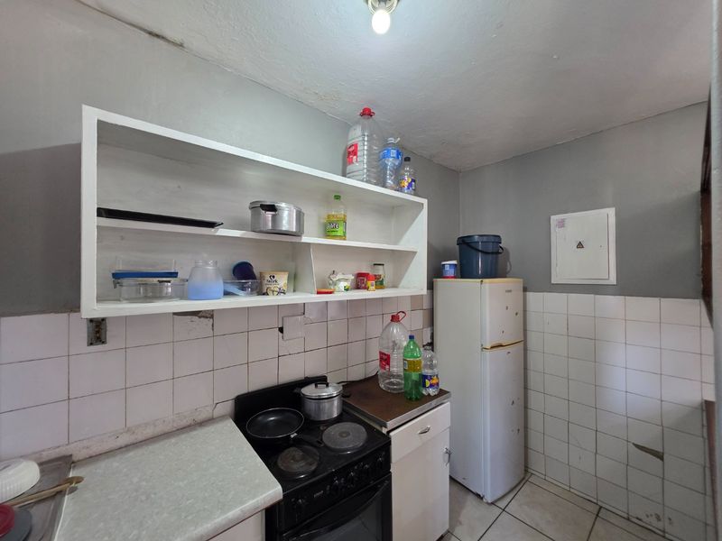 A compact kitchen featuring tiled splashbacks, built-in shelving, and an electric stove, requiring cosmetic updates to improve its overall condition and functionality.
