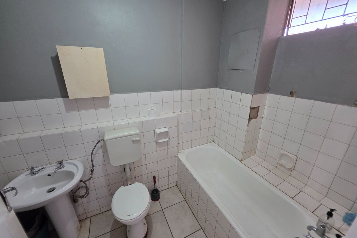 A dated bathroom featuring a pedestal basin, toilet, and bathtub with white wall tiling and grey painted upper walls, requiring cosmetic repairs.