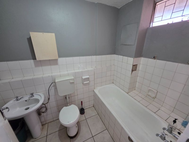 A dated bathroom featuring a pedestal basin, toilet, and bathtub with white wall tiling and grey painted upper walls, requiring cosmetic repairs.
