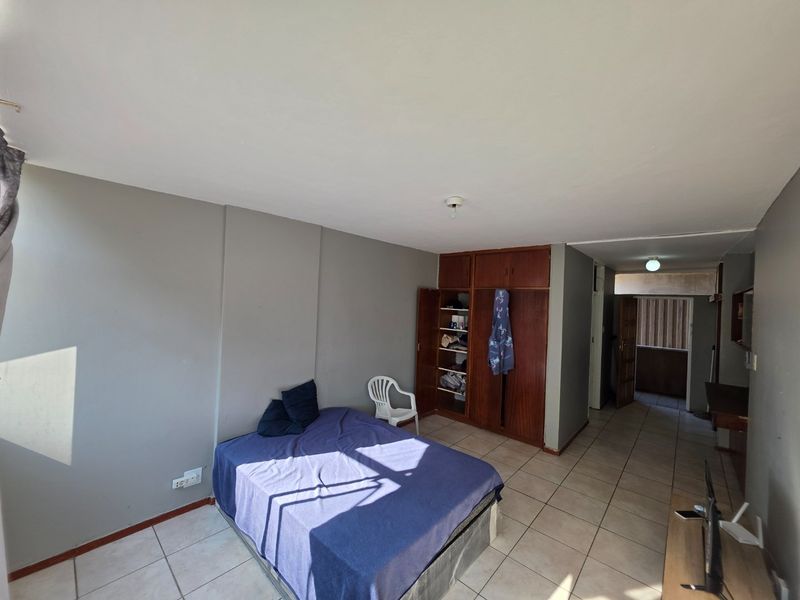 A bedroom featuring tiled flooring and a built-in wooden wardrobe, offering a functional space with potential for cosmetic updates.