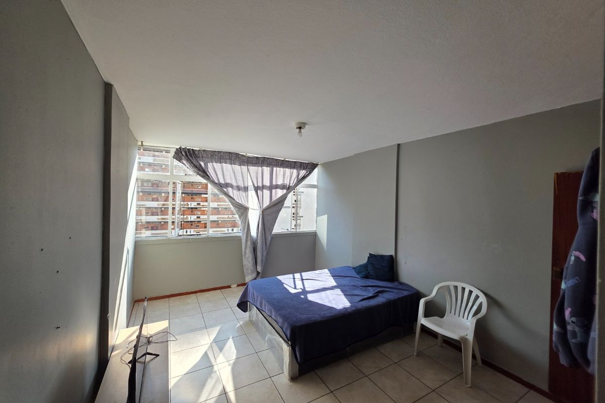 A bedroom featuring tiled flooring and large windows, providing natural light. The space requires cosmetic updates to the wall finishes.
