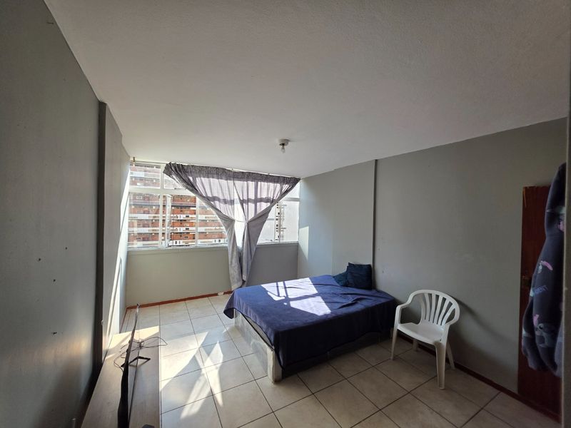 A bedroom featuring tiled flooring and large windows, providing natural light. The space requires cosmetic updates to the wall finishes.