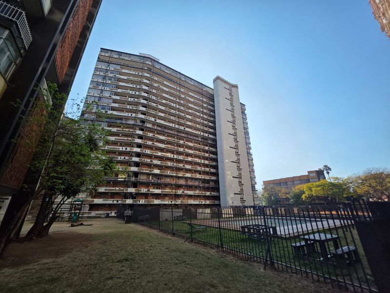 Exterior view of a high-rise apartment complex featuring a communal garden and a fenced swimming pool area.