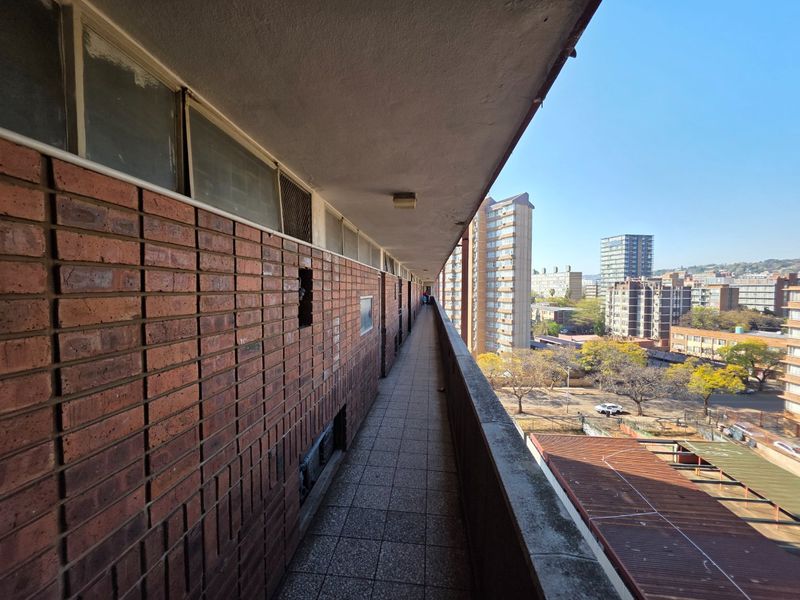 An exterior apartment balcony featuring exposed brick walls, tiled flooring, and a concrete balustrade, offering an elevated view of the surrounding urban neighborhood.