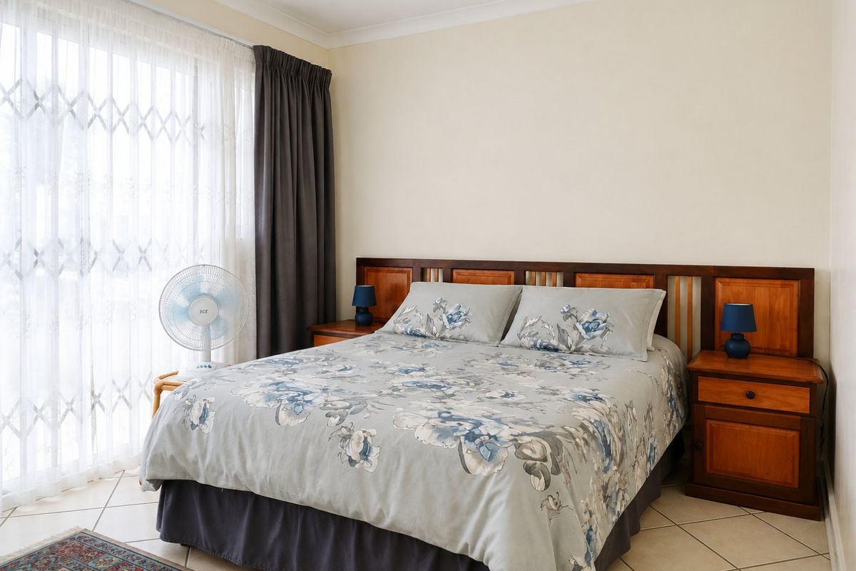 A bedroom featuring tiled flooring, a built-in wooden headboard, and a sliding glass door with a security gate providing natural light.