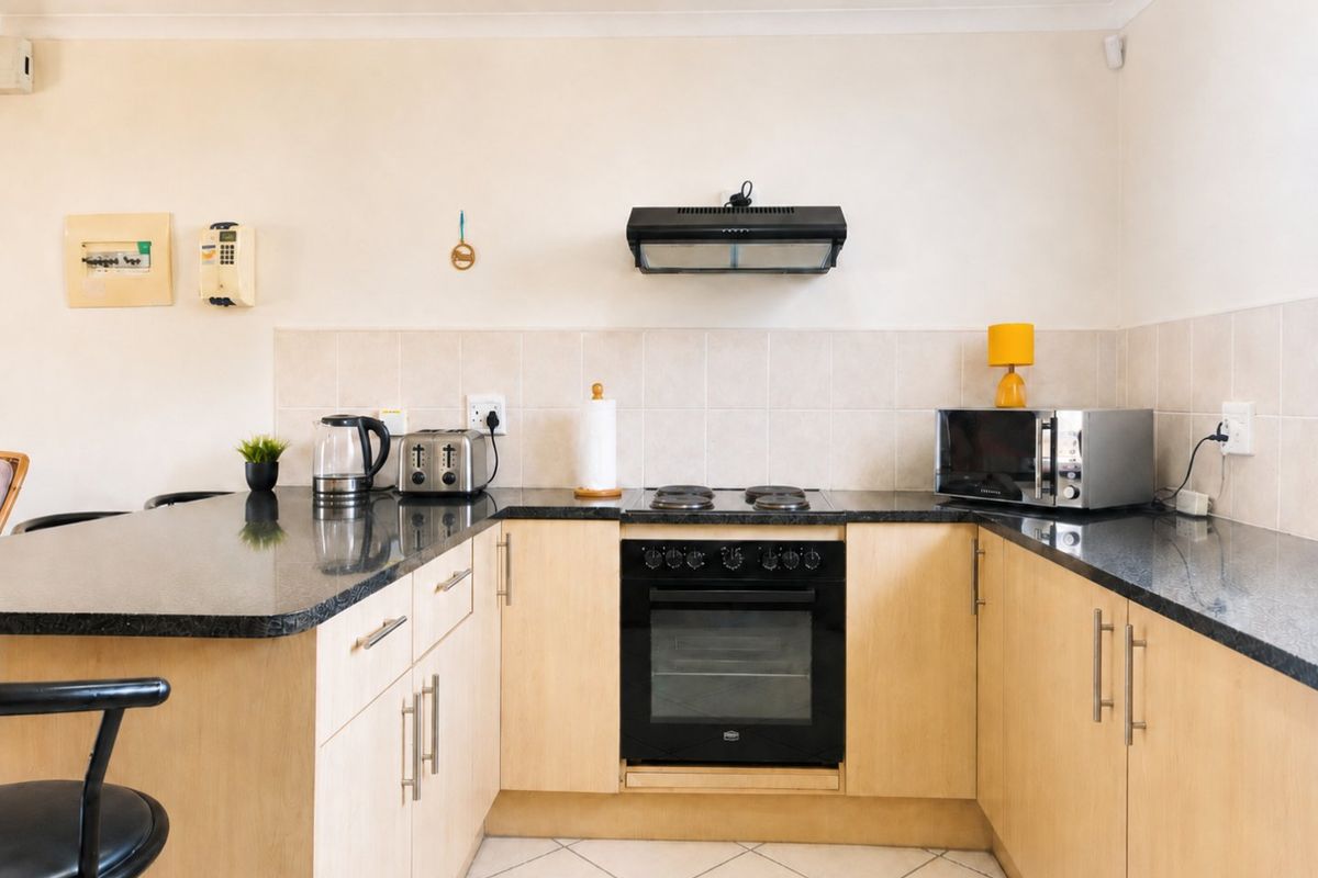 A functional kitchen featuring light wood cabinetry, dark granite countertops, a built-in oven, electric hob, and a tiled backsplash.