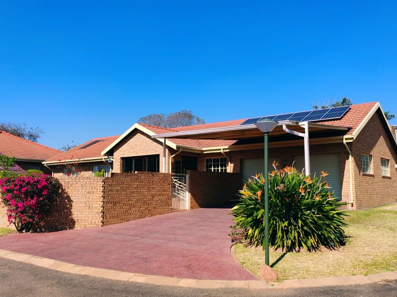 A well-maintained face brick house featuring a tiled roof, solar panels, a paved driveway, and a covered carport area.