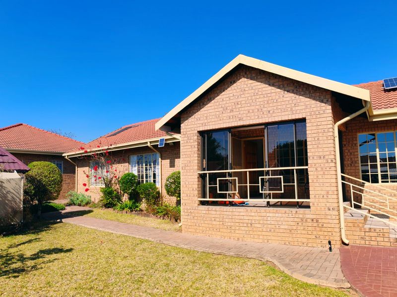 Rear view of a face brick house featuring a paved walkway, solar panels, and a covered patio area with sliding glass doors.