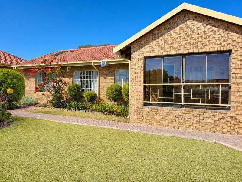 A well-maintained face brick house exterior featuring a tiled roof, paved walkway, and secure sliding windows set within a neat garden.