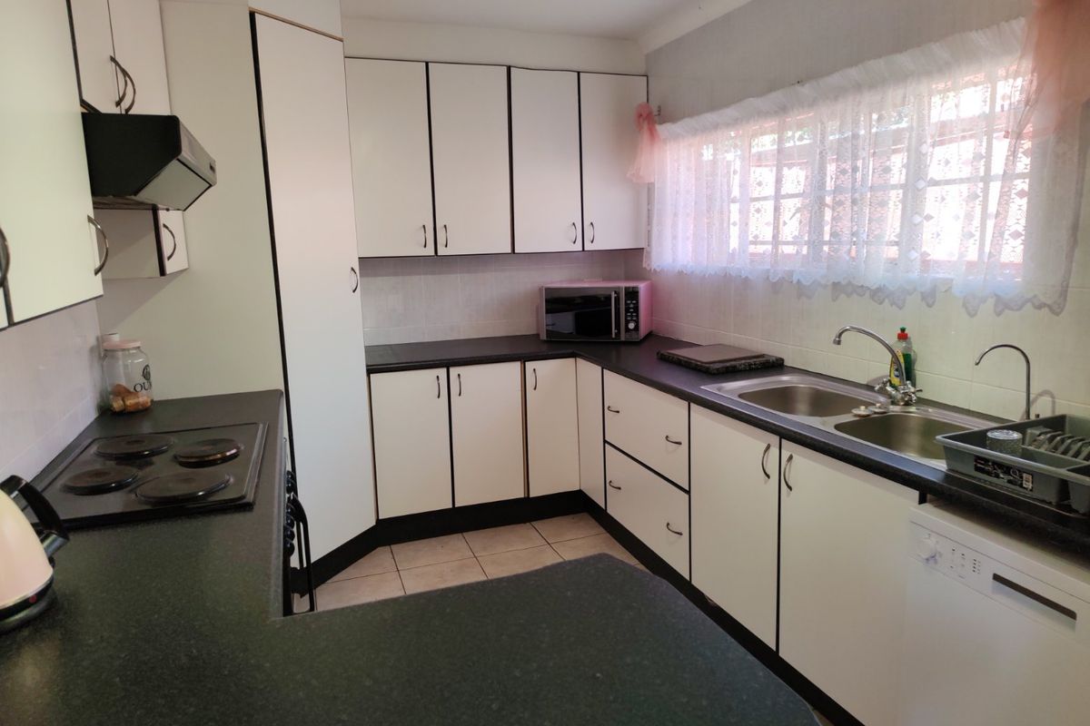 A functional kitchen featuring white cabinetry, dark laminate countertops, an electric hob with extractor, and a double basin sink with tiled backsplash.
