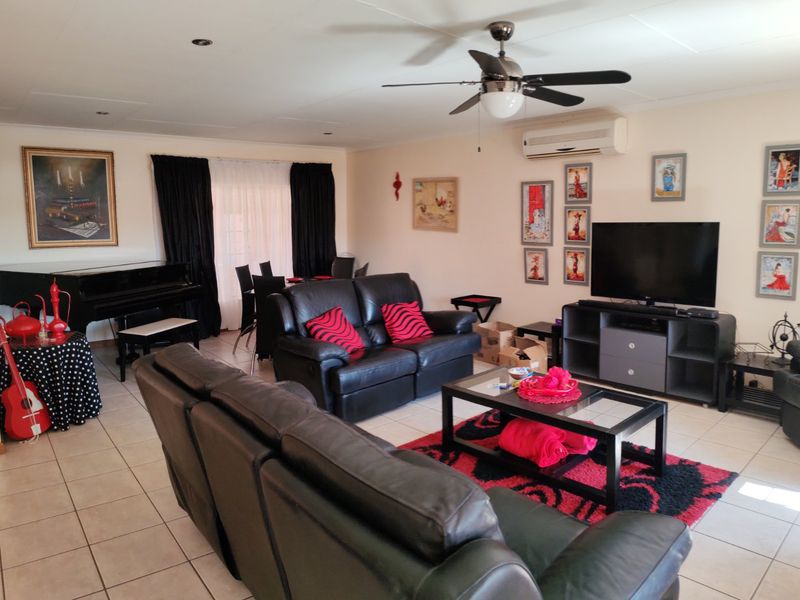 Spacious living room featuring tiled flooring, a ceiling fan, and a wall-mounted air conditioning unit, providing a comfortable and functional living space.