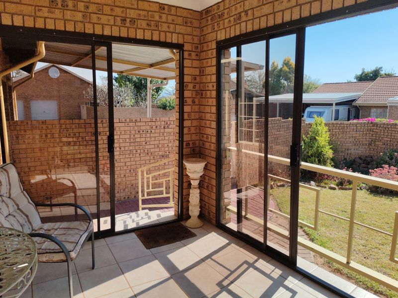 A covered patio area featuring tiled flooring, brick walls, and large sliding glass doors that open to the garden.