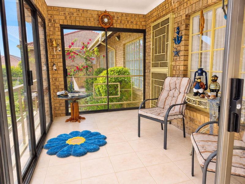 A bright, enclosed patio featuring exposed brick walls, tiled flooring, and large sliding glass doors that provide ample natural light and garden views.