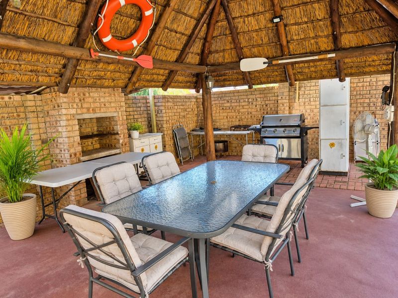 Covered outdoor entertainment area featuring a traditional thatched roof, exposed timber beams, and a built-in brick braai, perfect for alfresco dining.
