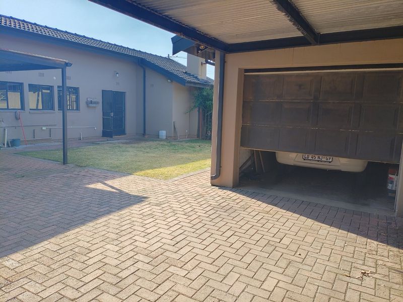 Rear exterior view featuring a paved driveway, carport, and garage access with a small lawn area.