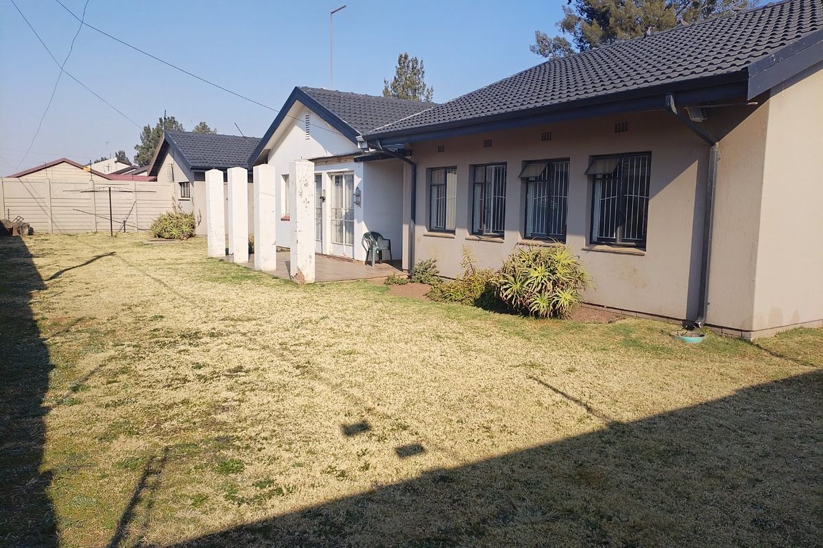 Rear view of the house featuring a tiled roof, security bars on windows, and a spacious backyard with a precast concrete boundary wall.