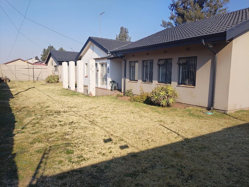 Rear view of the house featuring a tiled roof, security bars on windows, and a spacious backyard with a precast concrete boundary wall.