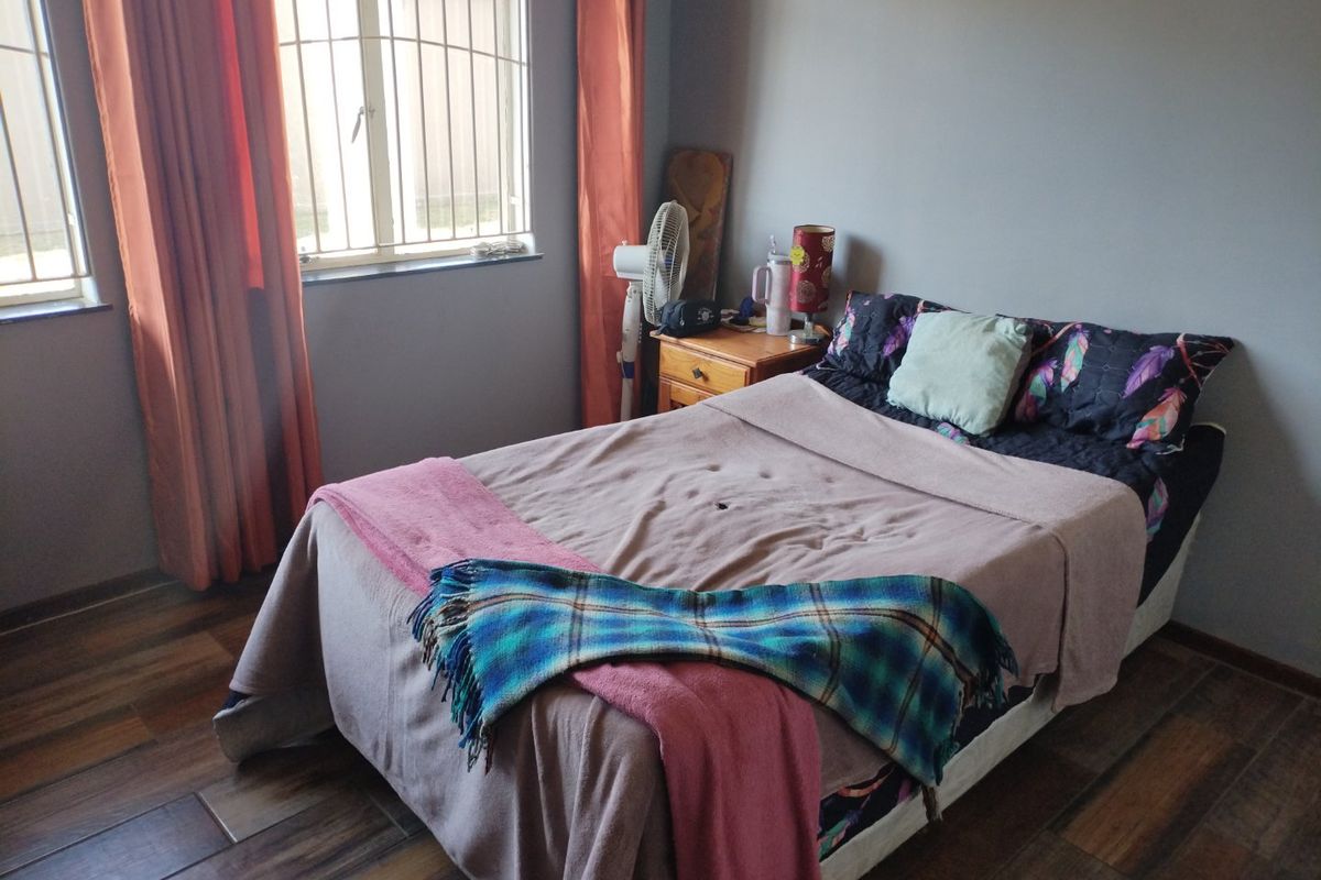 A bedroom featuring laminate flooring and windows fitted with security bars, providing a functional and private sleeping space.