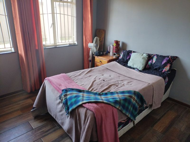 A bedroom featuring laminate flooring and windows fitted with security bars, providing a functional and private sleeping space.