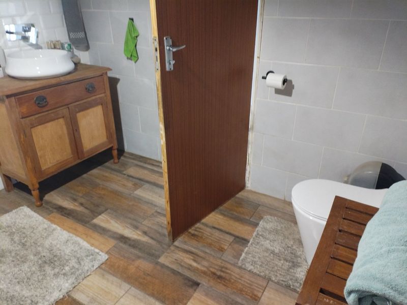 A bathroom featuring wood-look floor tiles, light grey wall tiles, a vessel sink on a wooden vanity, and a standard toilet.