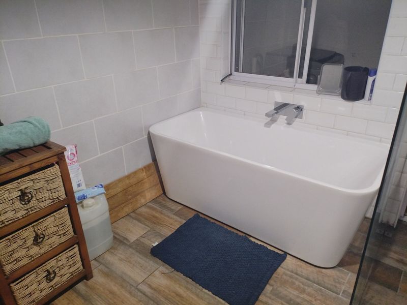 Modern bathroom featuring a clean white freestanding bathtub with chrome wall-mounted fixtures, complemented by subway tile backsplash and wood-look ceramic floor tiles.