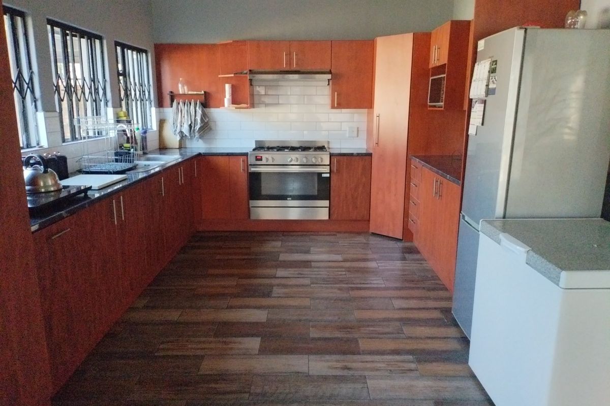 A functional kitchen featuring wood-finish cabinetry, granite countertops, a gas stove with extractor fan, and subway tile backsplash with wood-look tiled flooring.