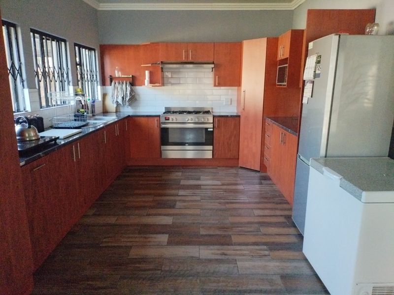 A functional kitchen featuring wood-finish cabinetry, granite countertops, a gas stove with extractor fan, and subway tile backsplash with wood-look tiled flooring.