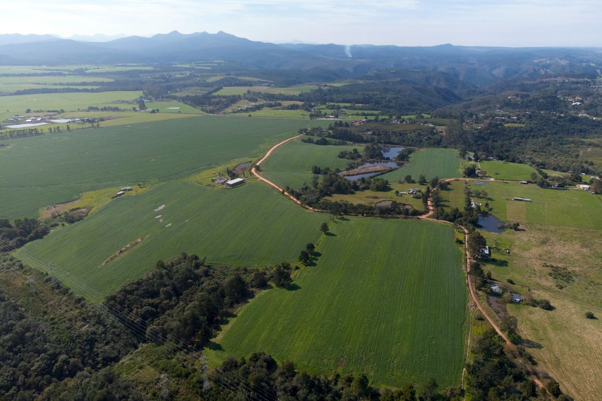 An expansive aerial view of a large farm property featuring cultivated green fields, internal access roads, multiple dams, and surrounding natural landscape.