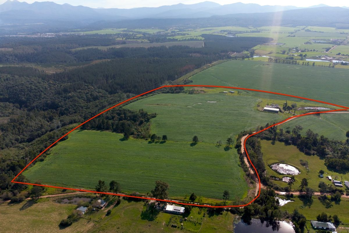 Aerial view of a large farm property featuring expansive green fields, farm buildings, access roads, and natural dams set against a mountain backdrop.