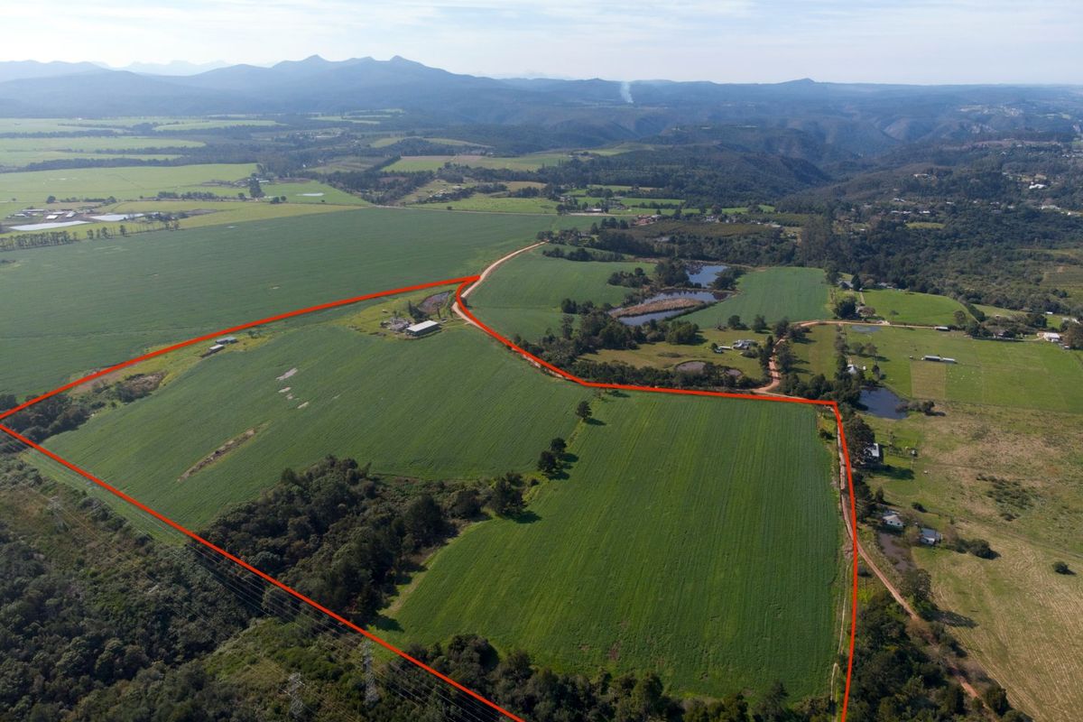 Aerial view of a large agricultural farm property featuring expansive green fields, multiple dams, and existing farm infrastructure with mountain views.