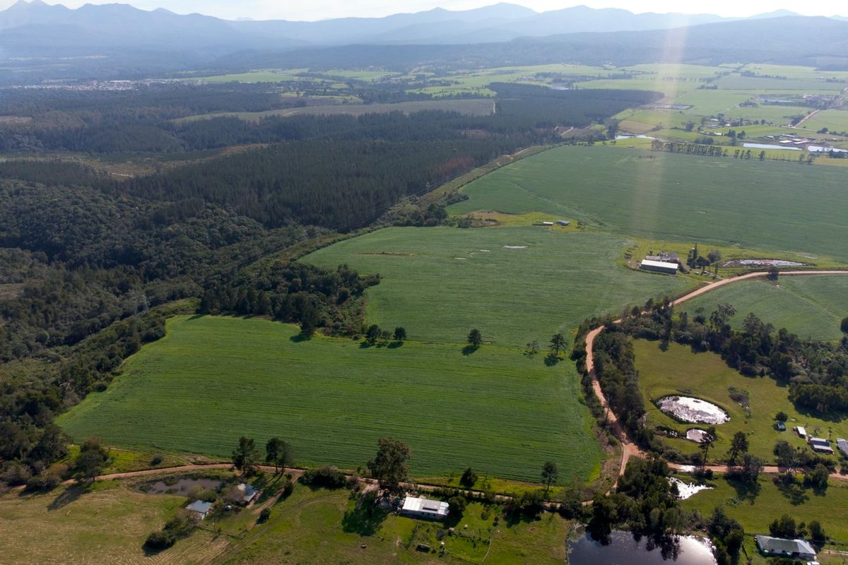 An aerial view of a large farm property featuring expansive green fields, dirt access roads, multiple farm dams, and various outbuildings.