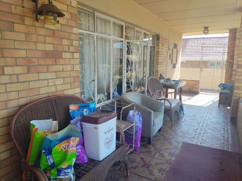 A covered patio area featuring patterned floor tiles, brick wall construction, and secure metal window grilles, providing a functional outdoor transition space.