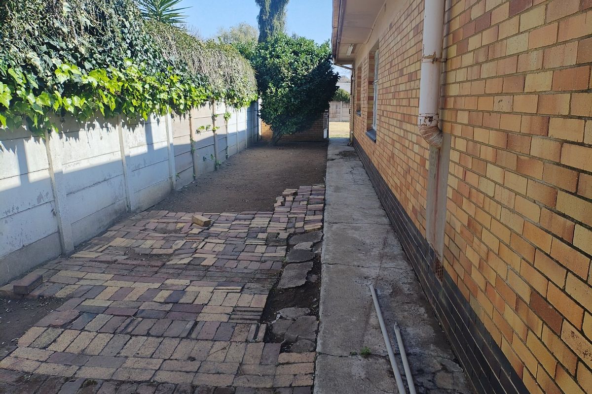 Side exterior area featuring a brick wall, concrete pathway, and a paved section requiring maintenance and repair.