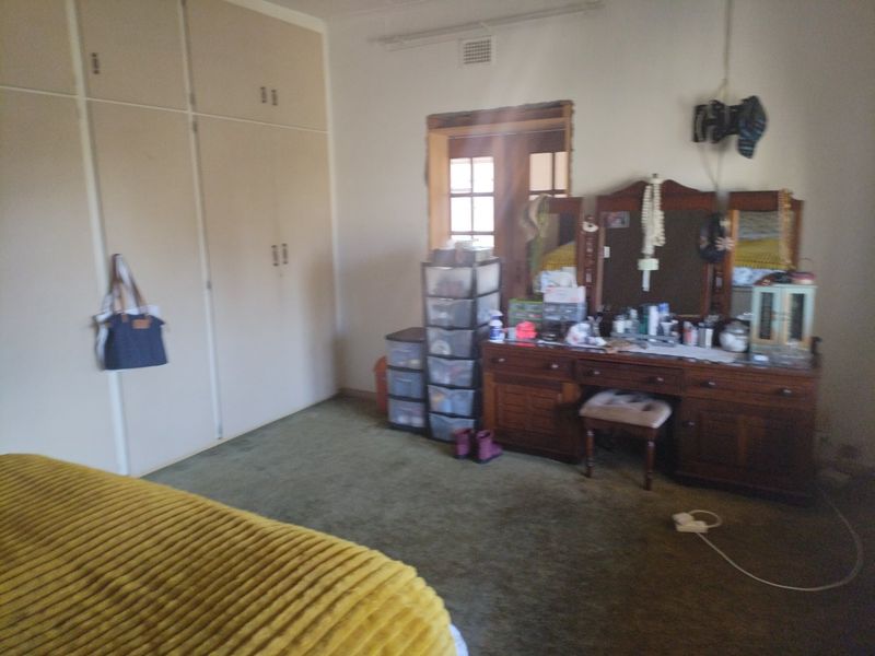 A bedroom featuring built-in cupboards and carpet flooring, currently requiring cosmetic updates to the door frame and general finishes.