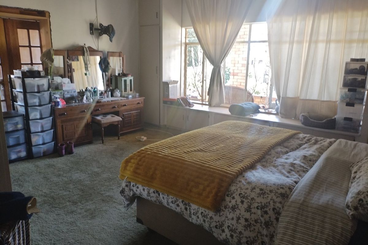 Spacious bedroom featuring built-in cupboards, a window seat, and carpet flooring, offering potential for modernization and aesthetic updates.