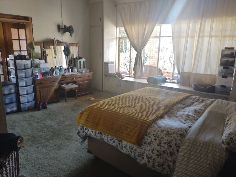 Spacious bedroom featuring built-in cupboards, a window seat, and carpet flooring, offering potential for modernization and aesthetic updates.