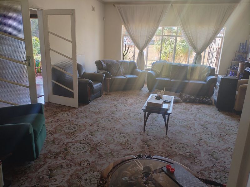 Spacious living room featuring patterned wall-to-wall carpeting, large windows with security bars, and an internal glass-panelled door leading to an outdoor area.
