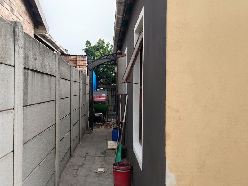 A narrow side walkway featuring a precast concrete boundary wall and paved flooring, providing access along the side of the house.