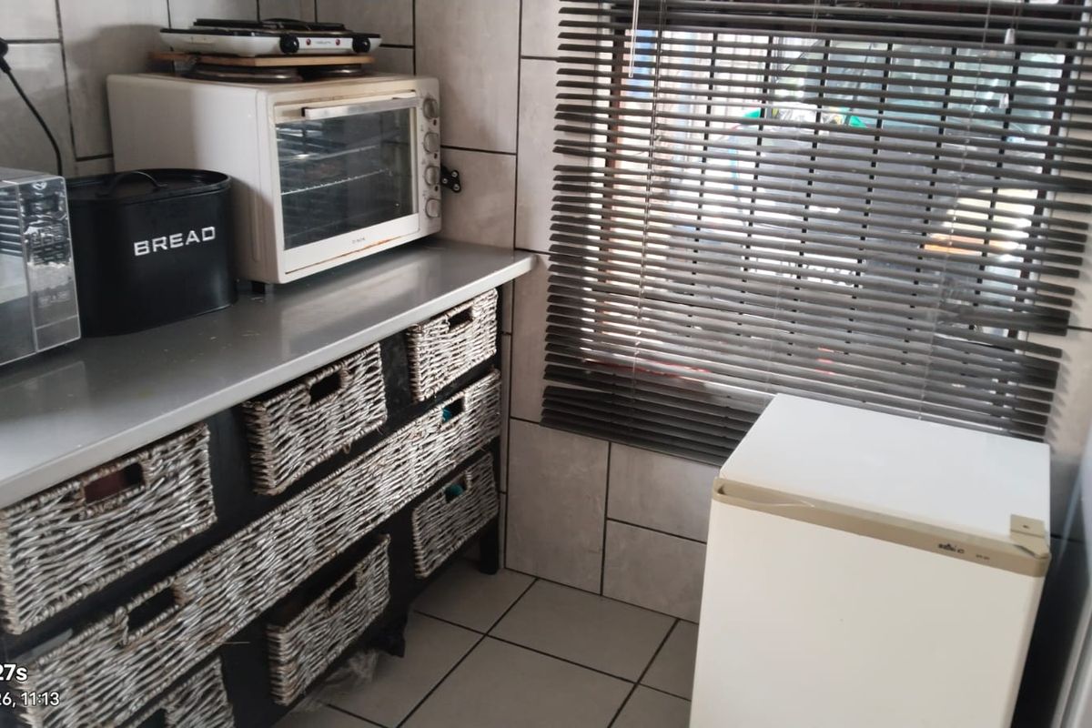 A functional kitchen area featuring tiled walls and flooring, a countertop, and venetian blinds over the window.