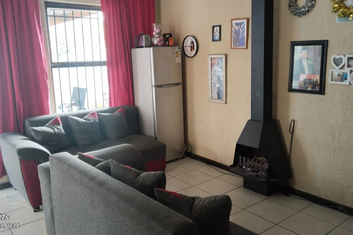 Living room featuring tiled flooring and a black metal freestanding fireplace, with natural light entering through a window fitted with security bars.