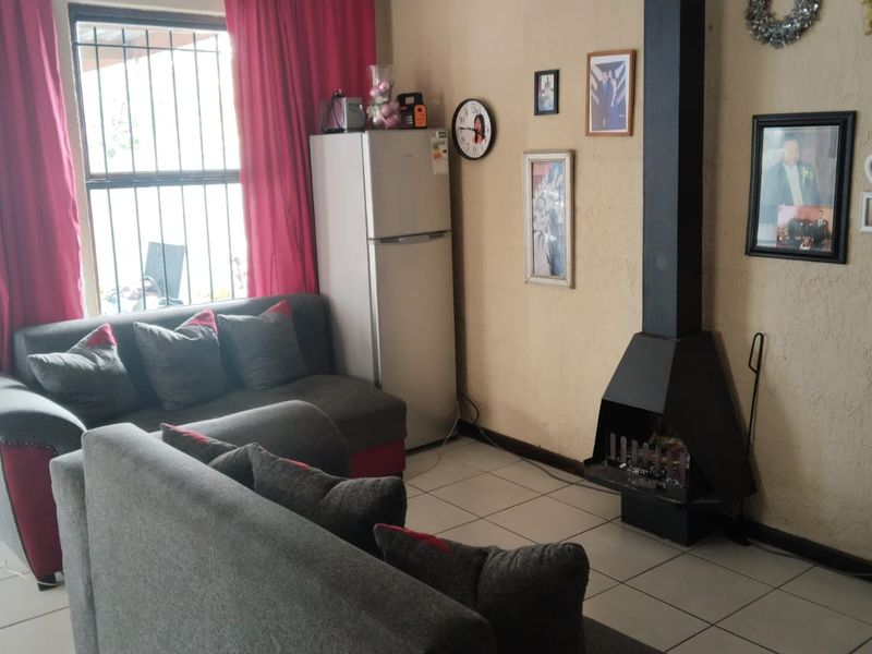 Living room featuring tiled flooring and a black metal freestanding fireplace, with natural light entering through a window fitted with security bars.