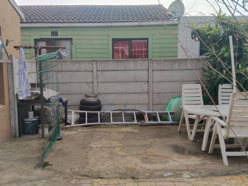 A rear exterior area featuring a concrete patio and boundary wall, providing a functional outdoor space with potential for landscaping and improvement.
