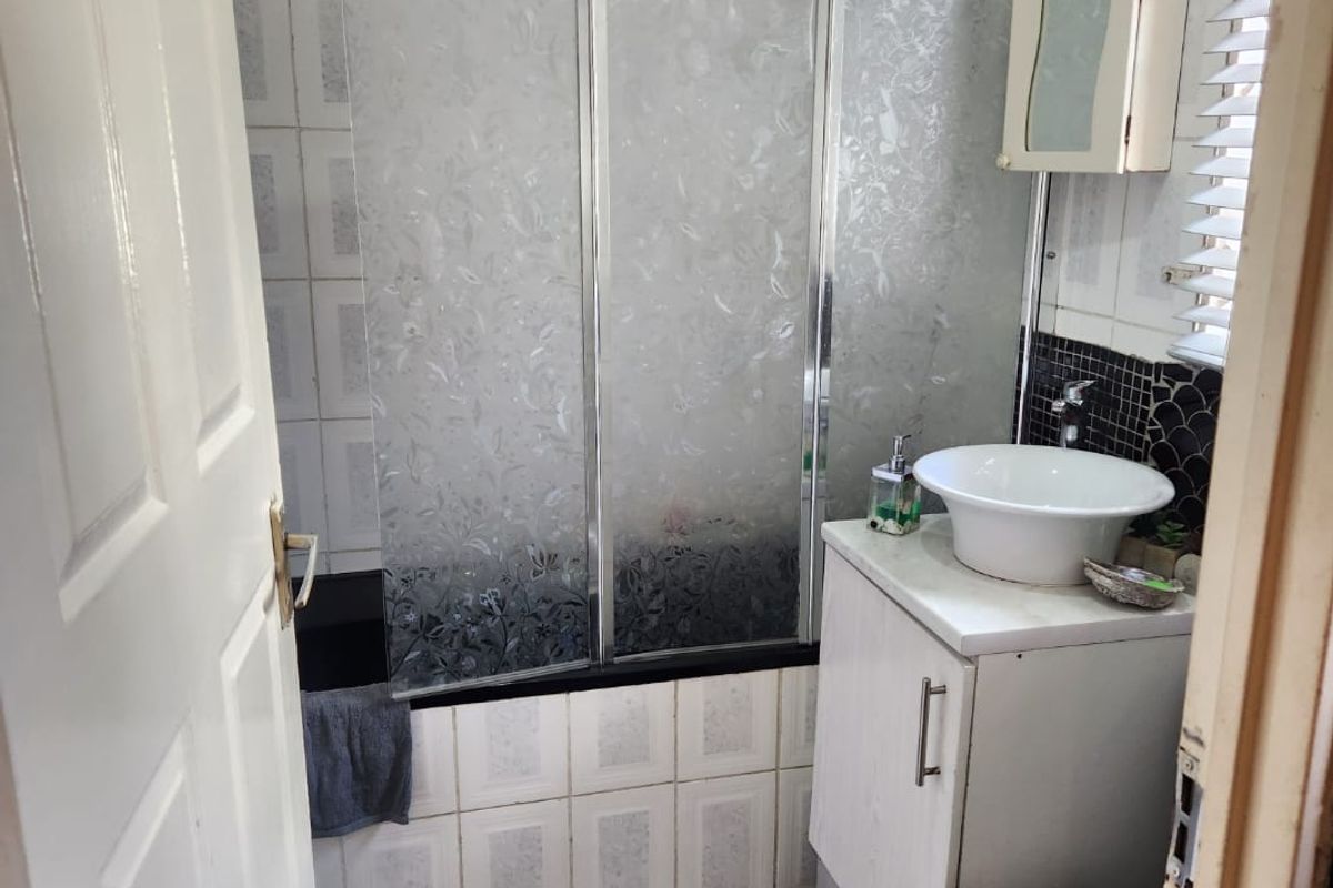 Compact bathroom featuring a bathtub with a shower screen, a vessel sink vanity, and tiled finishes throughout.