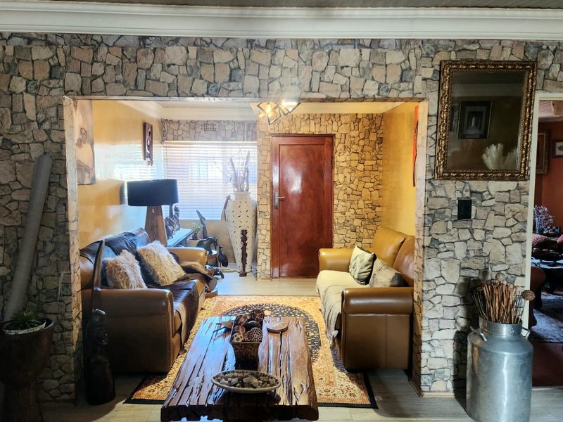 A living room featuring stone-clad feature walls, laminate flooring, and a timber door, offering a rustic aesthetic with potential for modern updates.
