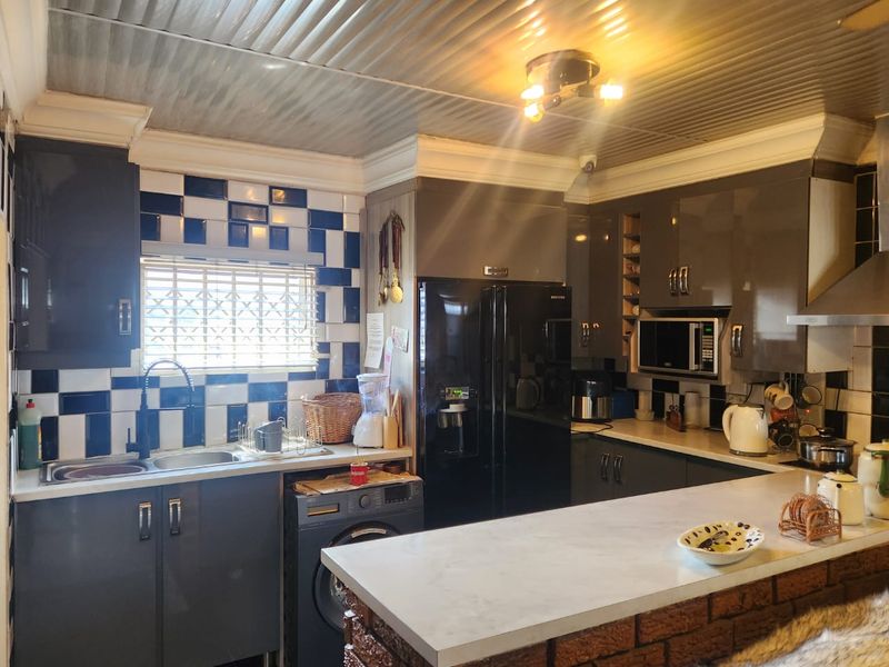 A functional kitchen featuring dark cabinetry, a breakfast bar with a brick base, tiled backsplash, and a distinctive corrugated metal ceiling.