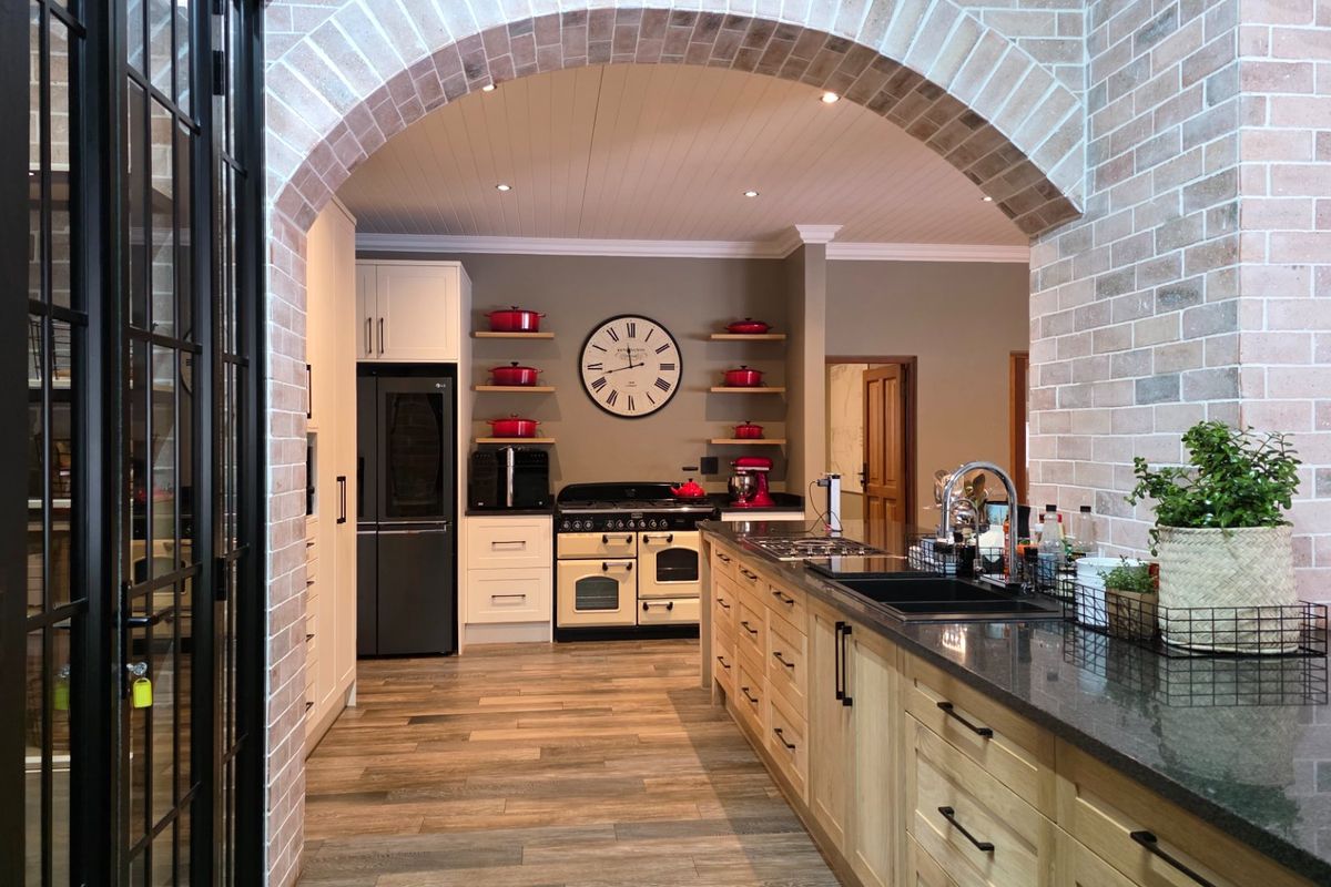 A beautifully appointed kitchen featuring a brick archway, a large central island with granite countertops, and a classic freestanding range cooker.
