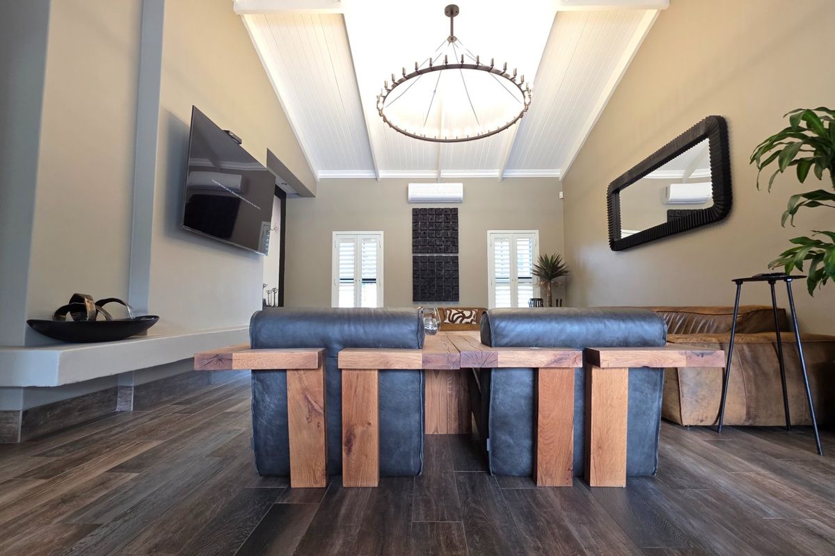 Spacious living room featuring a high vaulted ceiling, timber-look flooring, split-system air conditioning, and elegant shutter-style window treatments.