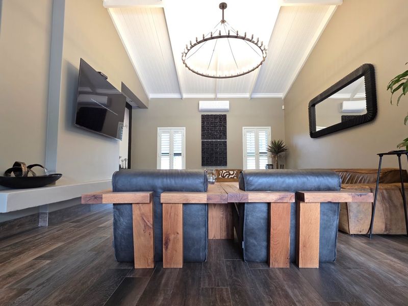Spacious living room featuring a high vaulted ceiling, timber-look flooring, split-system air conditioning, and elegant shutter-style window treatments.